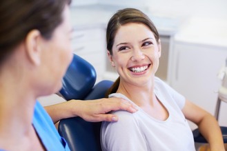 Smiling woman sitting in dental chair, talking with dentist about oral hygiene and preventive dental care.